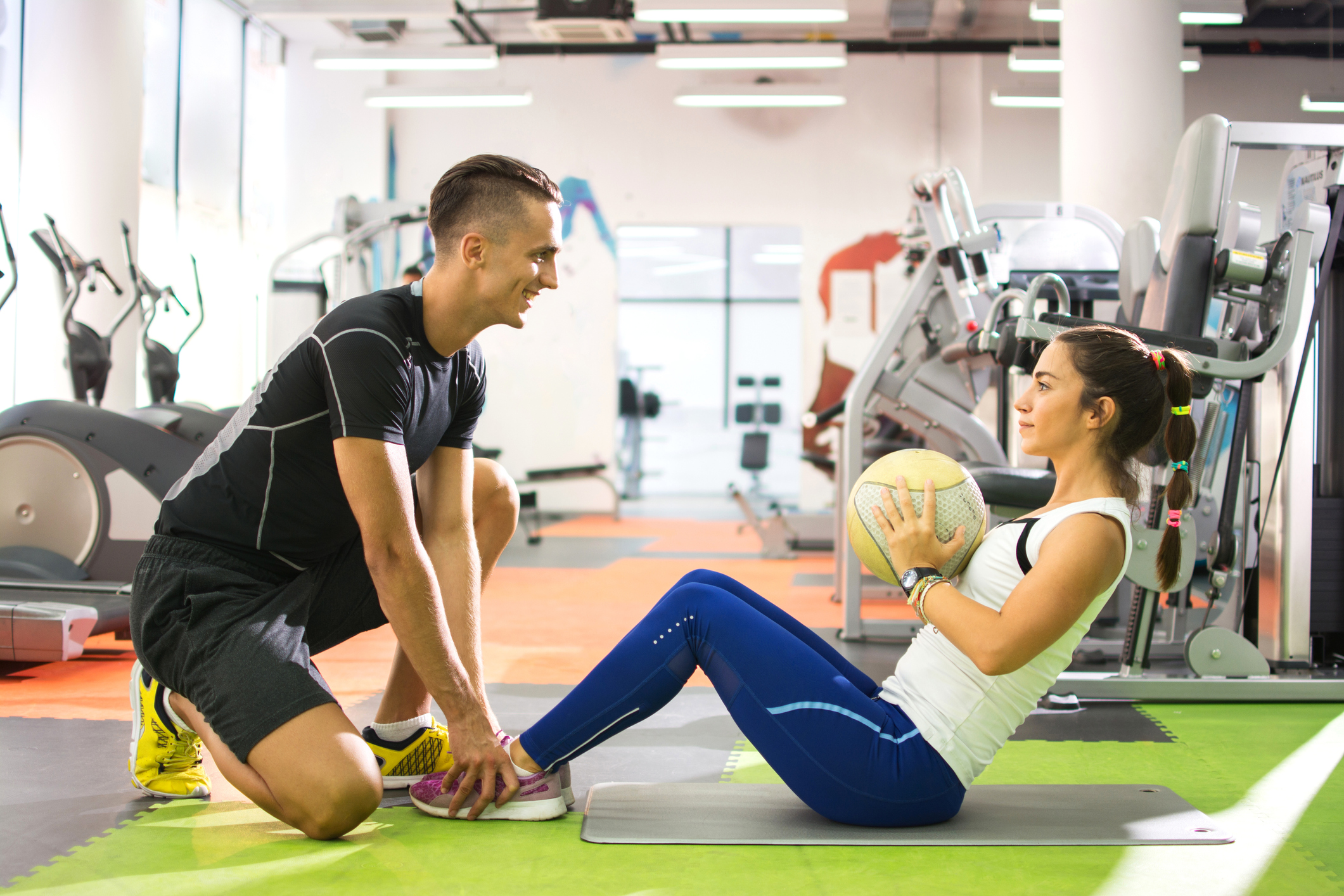Female client doing abdominal crunches with ball while her personal trainer assisting her