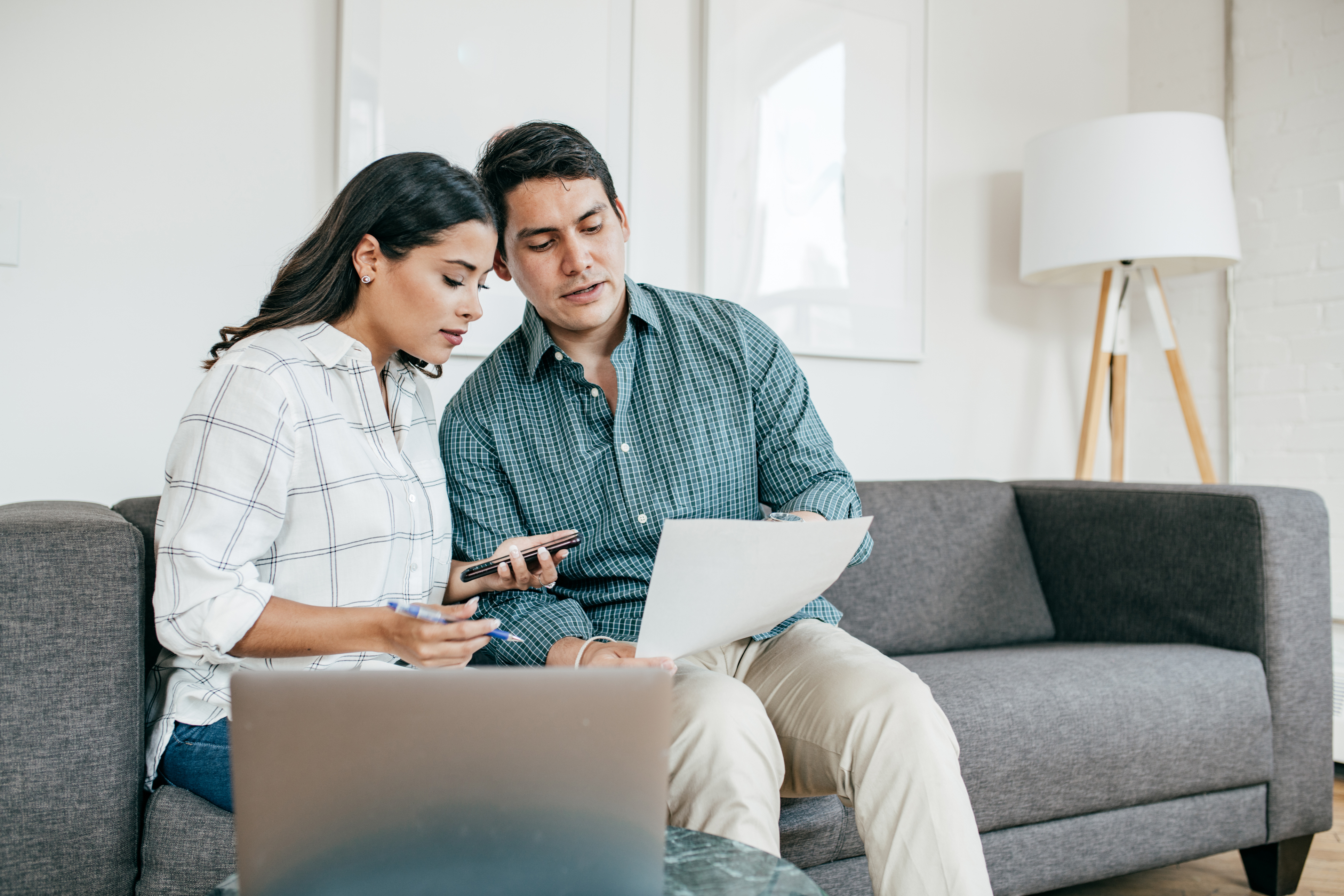 A couple sits on a couch reading a piece of paper